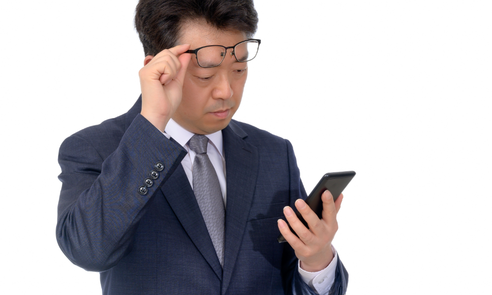 スマートフォンの文字が見えづらいのでメガネを外す老眼の男性